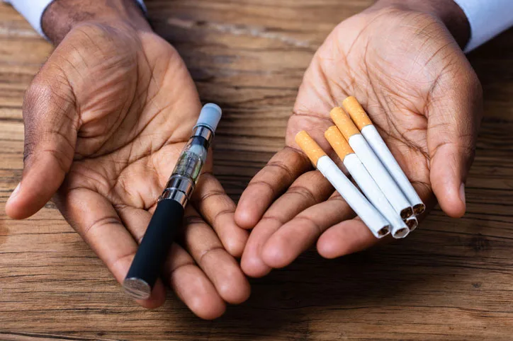 Hands holding a vape pen and cigarettes