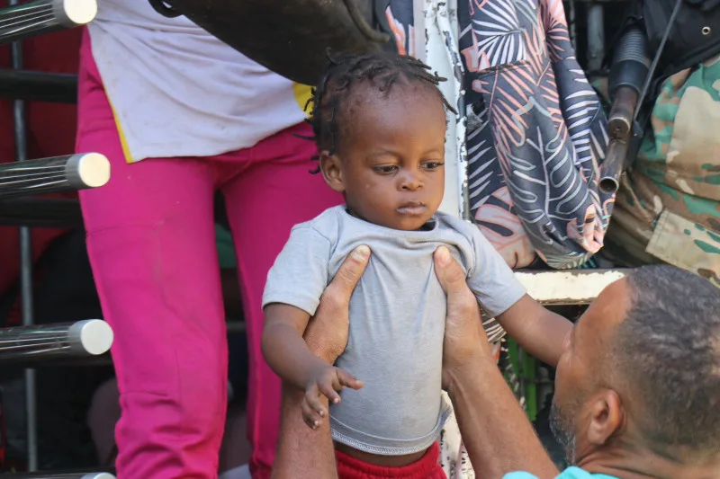 Hombre bajando a niño de camión de Migración.