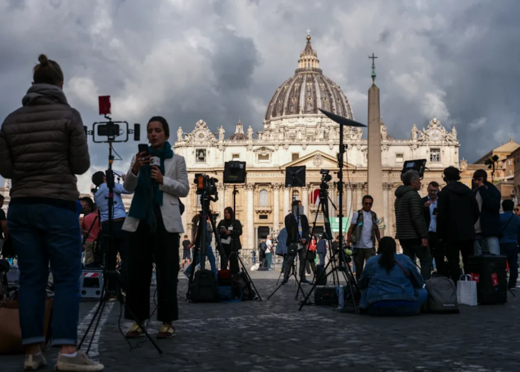 Los periodistas trabajan en la Plaza de San Pedro, con la basílica de San Pedro al fondo, antes de la segunda sesión de votación del cónclave, en el Vaticano, el 8 de mayo de 2025.