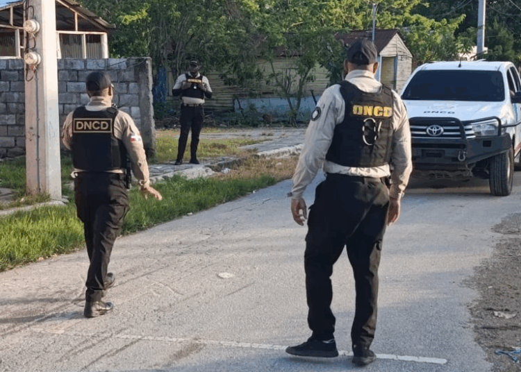 Agentes de la DNCD o la policía realizando una captura, con paquetes de drogas incautadas y armas, representando un operativo antidrogas.