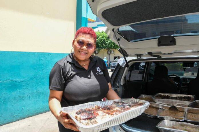 Persona recibiendo una ración de comida preparada, con logo de Comedores Económicos