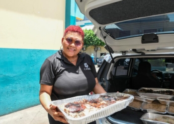 Persona recibiendo una ración de comida preparada, con logo de Comedores Económicos
