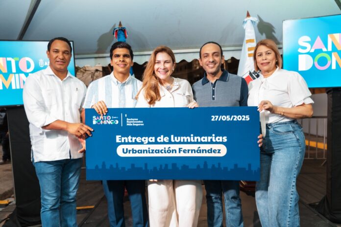 Carolina Mejía entregando luminarias o con residentes de la Urbanización Fernández, en un evento nocturno con iluminación LED.