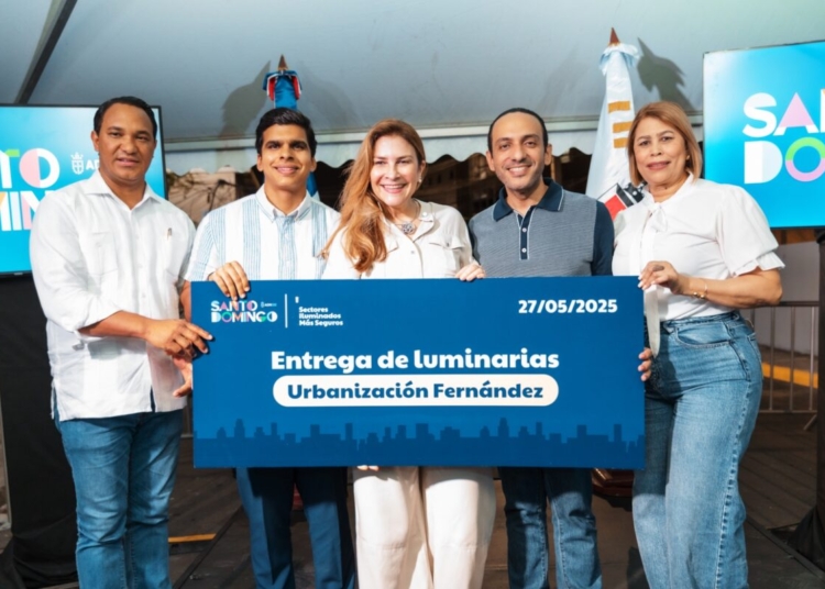 Carolina Mejía entregando luminarias o con residentes de la Urbanización Fernández, en un evento nocturno con iluminación LED.