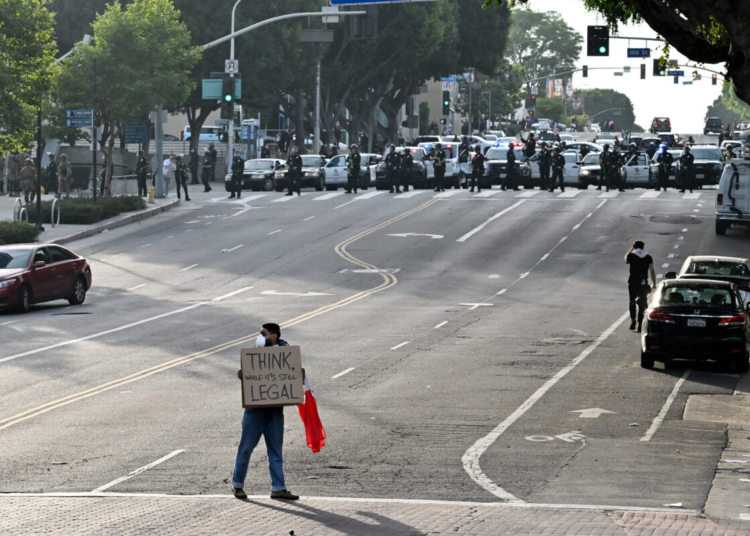A protestor holds a sign reading "think, while it's still legal," as police move into position to clear the streets on june 14, 2025 in los angeles, california after the "no kings" demonstration. Tens of thousands of protesters rallied nationwide saturday against donald trump ahead of a huge military parade on the us president's 79th birthday -- as the killing of a democratic lawmaker underscored the deep divisions in american politics. "no kings" demonstrators took to the streets in new york, los angeles, chicago, philadelphia, houston, atlanta and hundreds of other cities across the united states to condemn what they call trump's dictatorial overreach. (photo by robyn beck / afp)