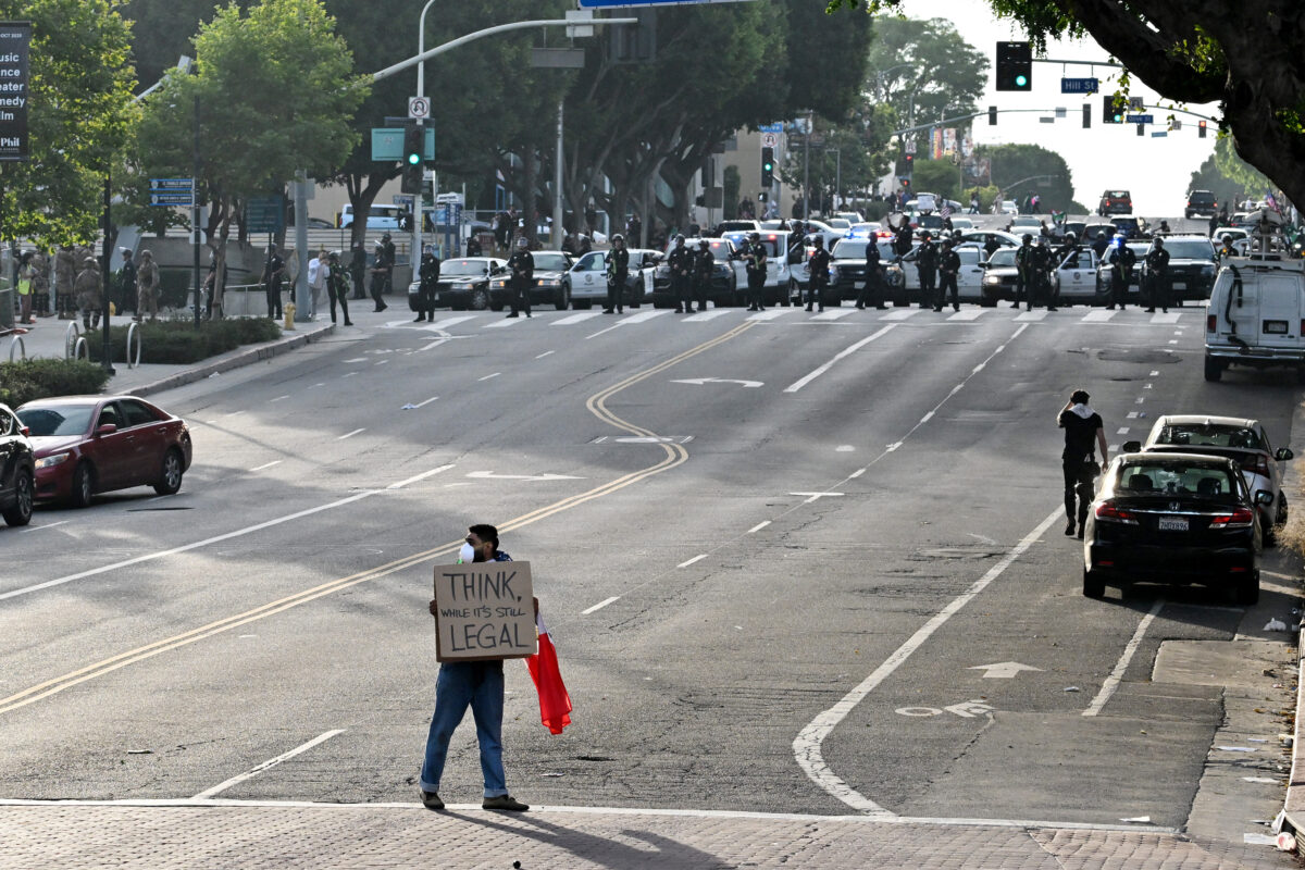 A protestor holds a sign reading "think, while it's still legal," as police move into position to clear the streets on june 14, 2025 in los angeles, california after the "no kings" demonstration. Tens of thousands of protesters rallied nationwide saturday against donald trump ahead of a huge military parade on the us president's 79th birthday -- as the killing of a democratic lawmaker underscored the deep divisions in american politics. "no kings" demonstrators took to the streets in new york, los angeles, chicago, philadelphia, houston, atlanta and hundreds of other cities across the united states to condemn what they call trump's dictatorial overreach. (photo by robyn beck / afp)