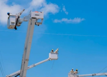 Técnicos de eted realizando labores de mantenimiento en una torre de transmisión eléctrica al atardecer.