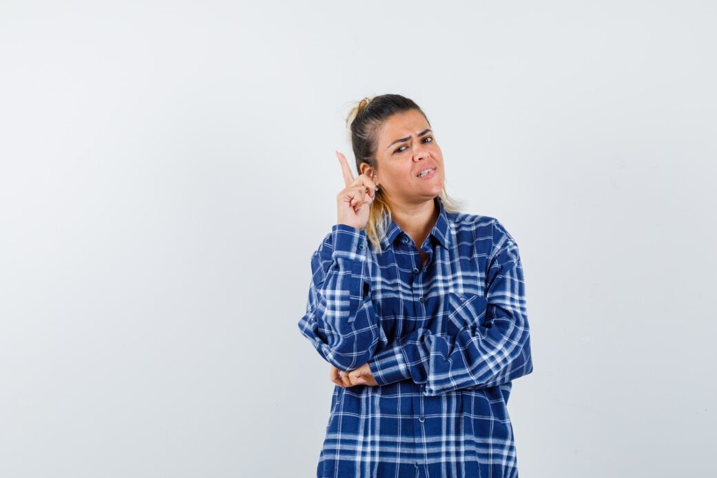 young lady in checked shirt pointing up and looking indecisive , front view.